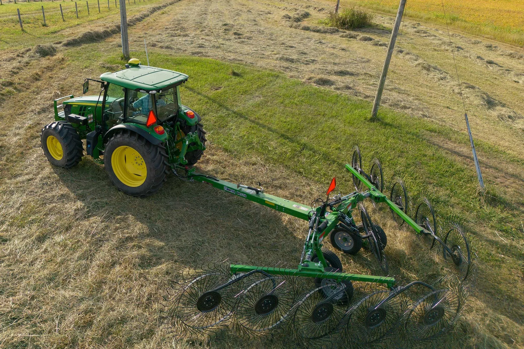 Top view of a 5M tractor pulling a WR3210 wheel rake across cut hay field