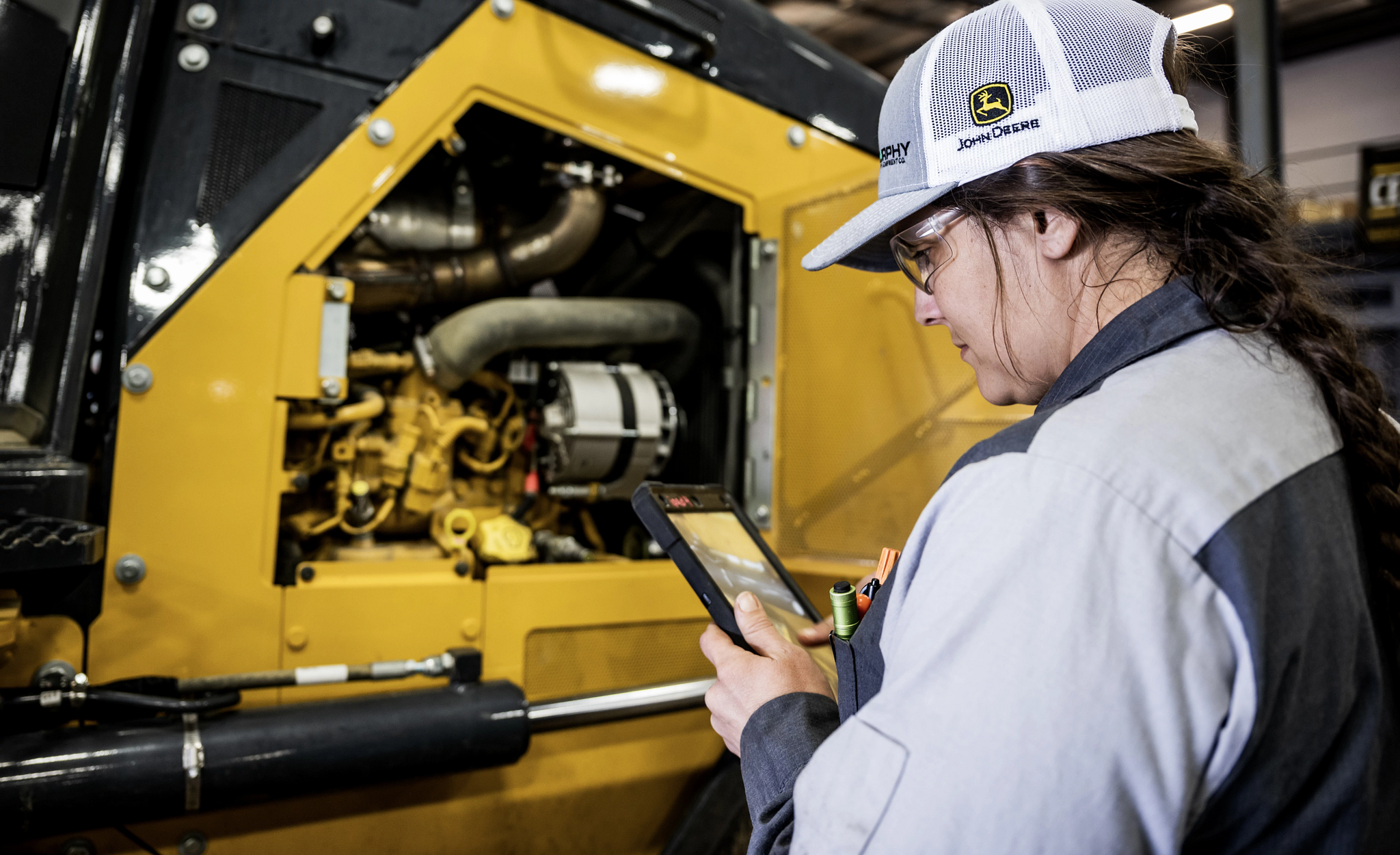 John Deere service technician looking at tablet and assessing engine