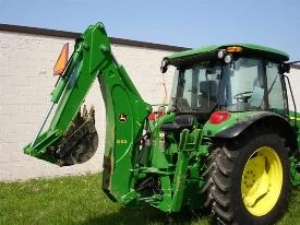 Rear right view of a 595 backhoe on grass in front of a wall with boom and bucket curled up in transport mode