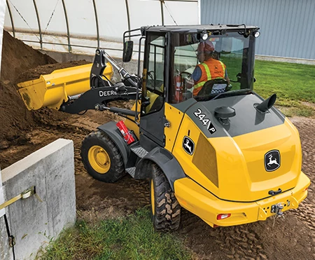 Rear left view of a 244 P-Tier compact wheel loader handling dirt with Articulation Plus™ steering in action