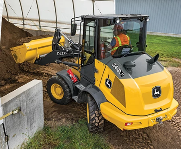 Rear left view of a 244 P-Tier compact wheel loader handling dirt with Articulation Plus™ steering in action