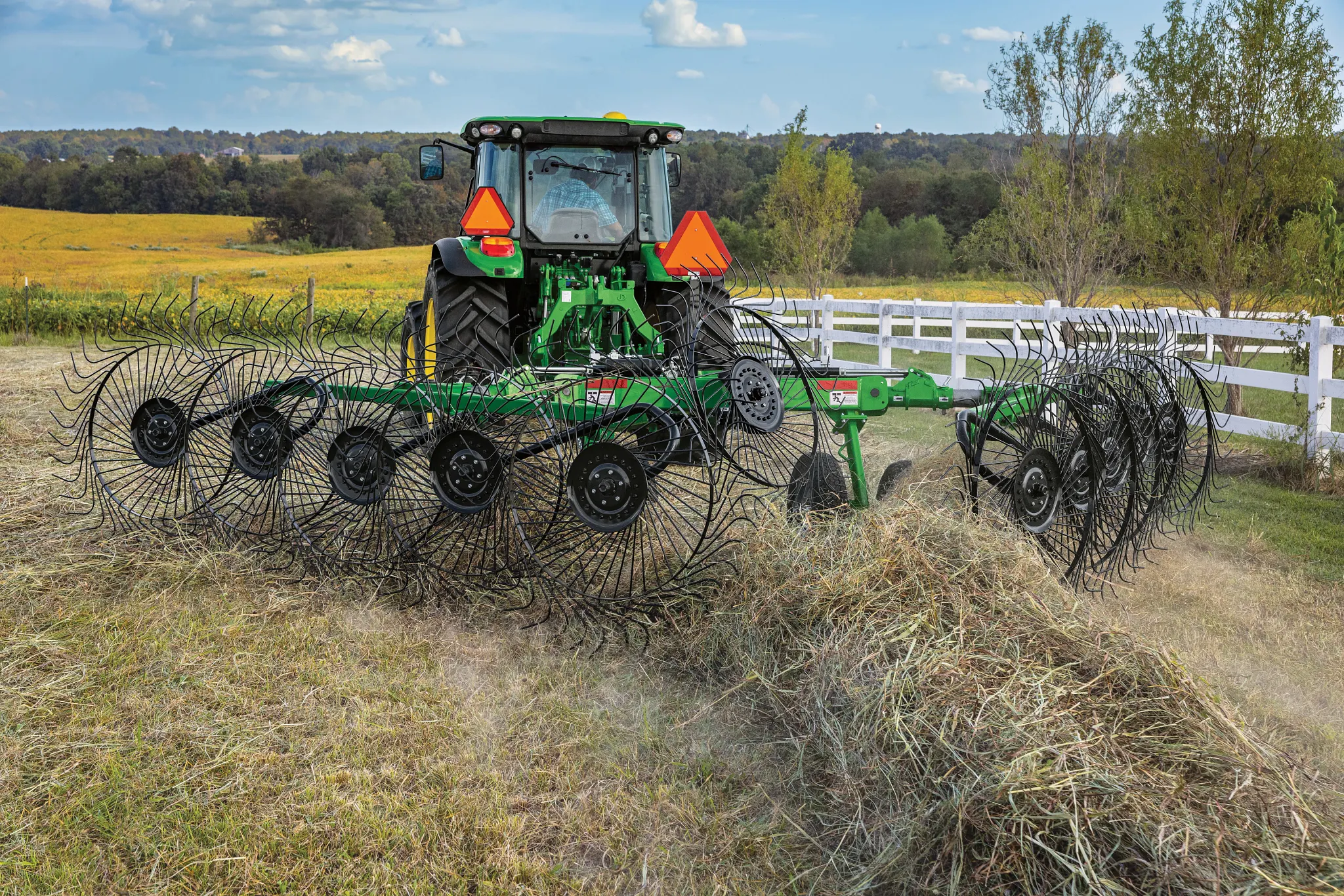 Rear view of a 5M tractor using a WR3210 wheel rake in the country