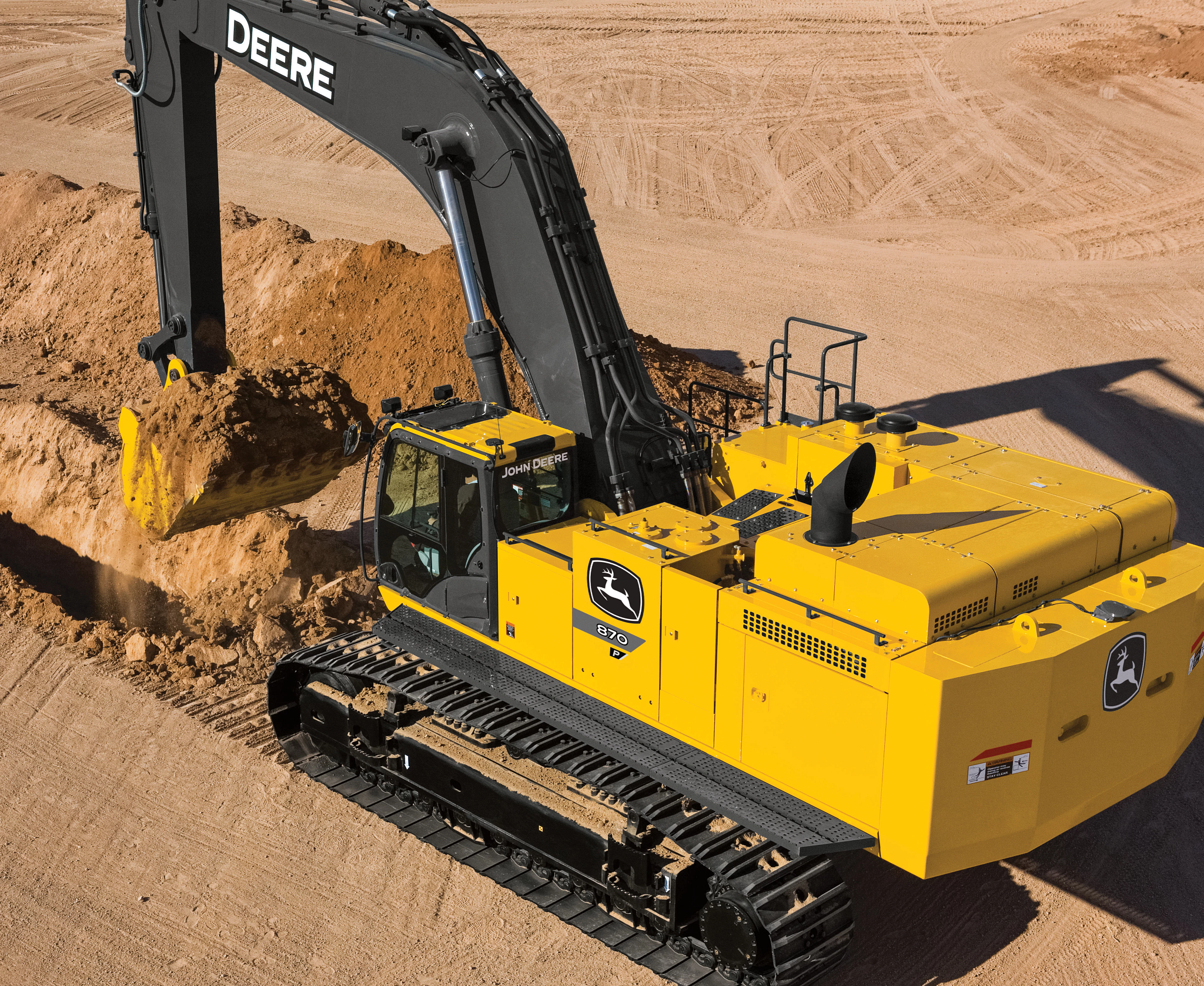 Large yellow John Deere excavator (model 470) with a black arm scooping a bucket of soil at a sandy construction site