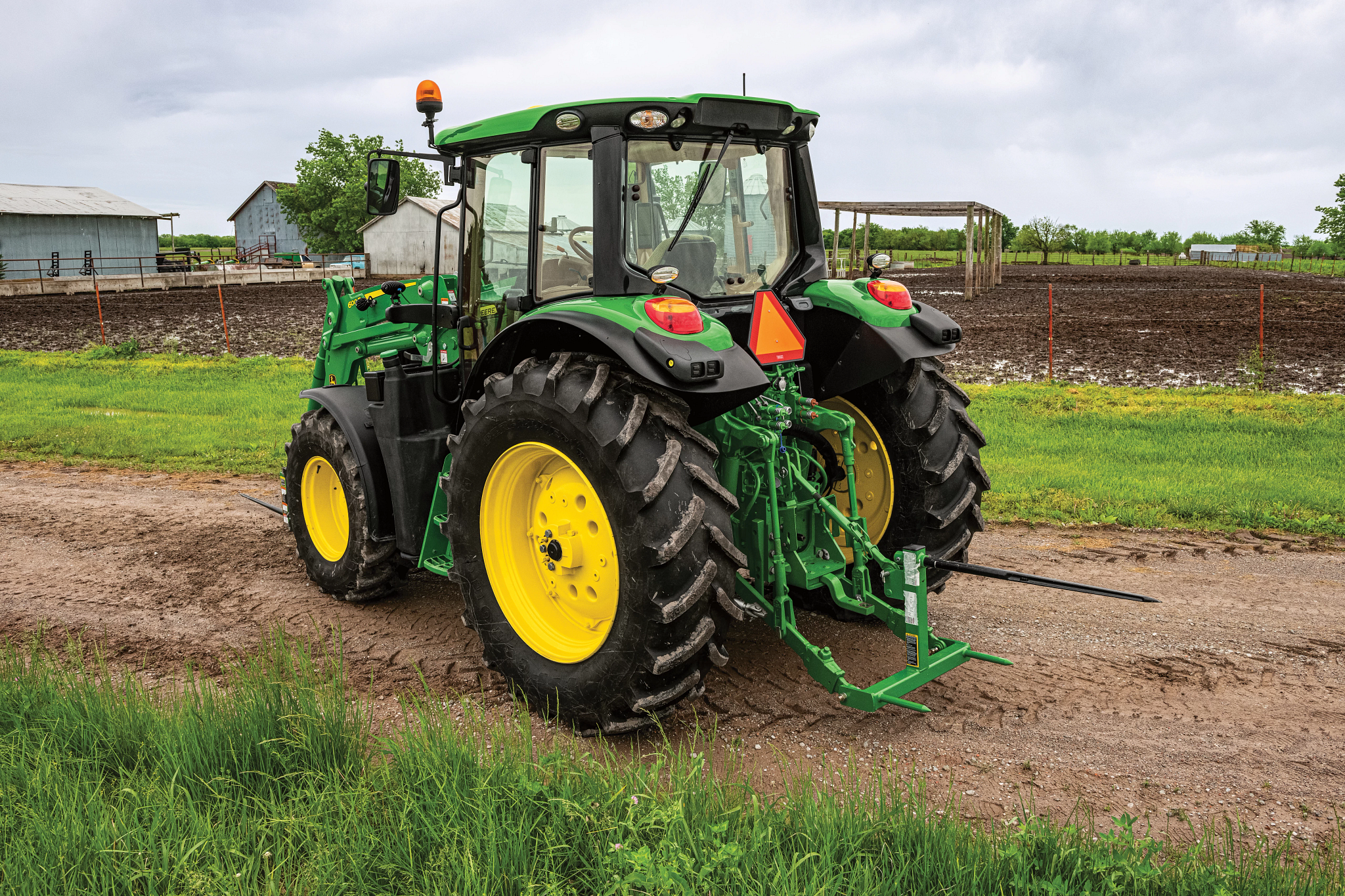 A tractor with a bale spear on a dirt road near crop fields