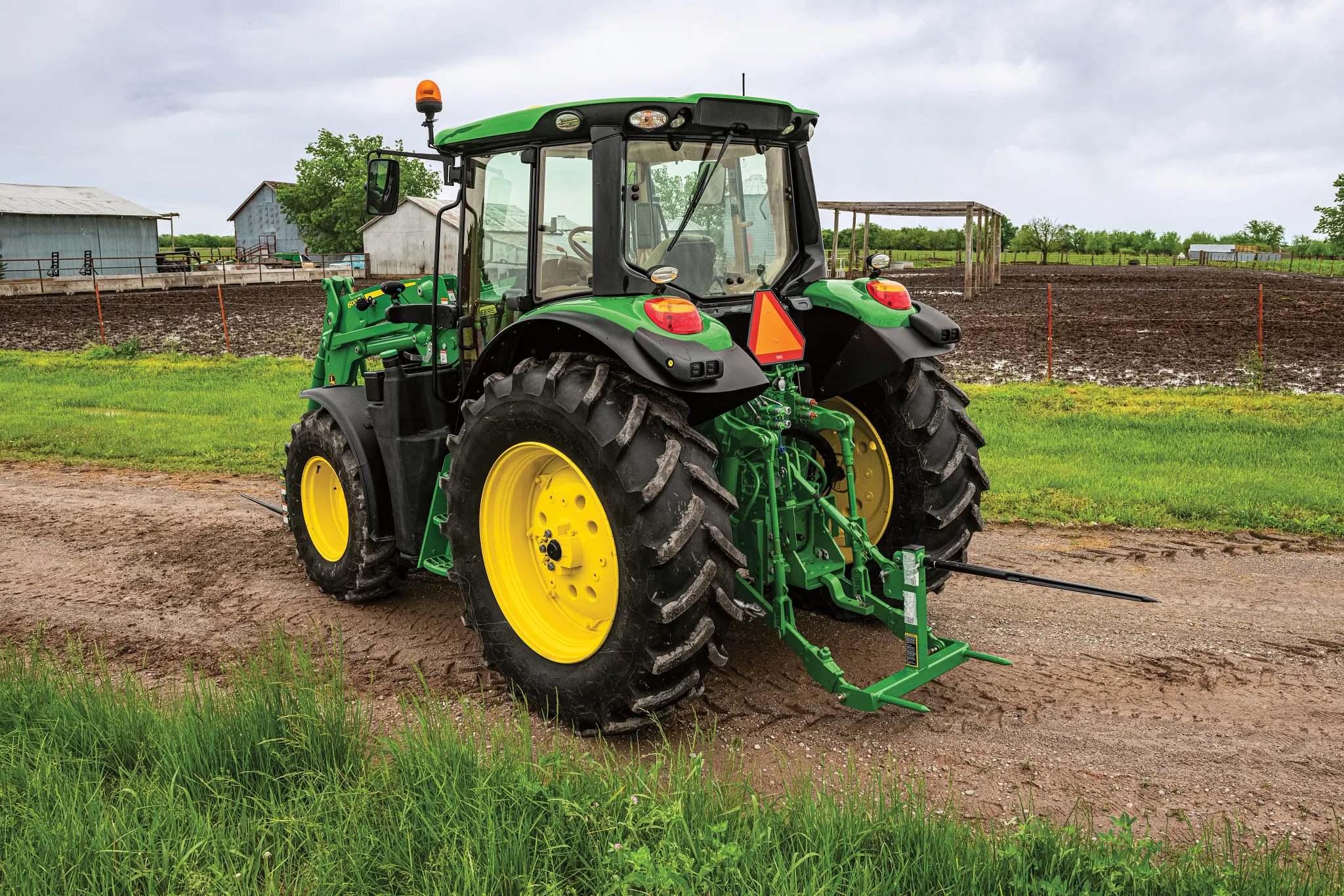 A tractor with a bale spear on a dirt road near crop fields
