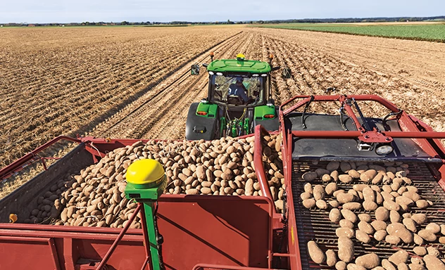 Rear overhead view of a tractor pulling a potato harvester in a field.
