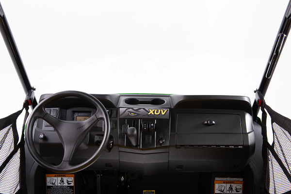 A straight-on view of the dashboard and steering wheel of a John Deere XUV, showing central controls, gauges, a storage compartment, and mesh doors