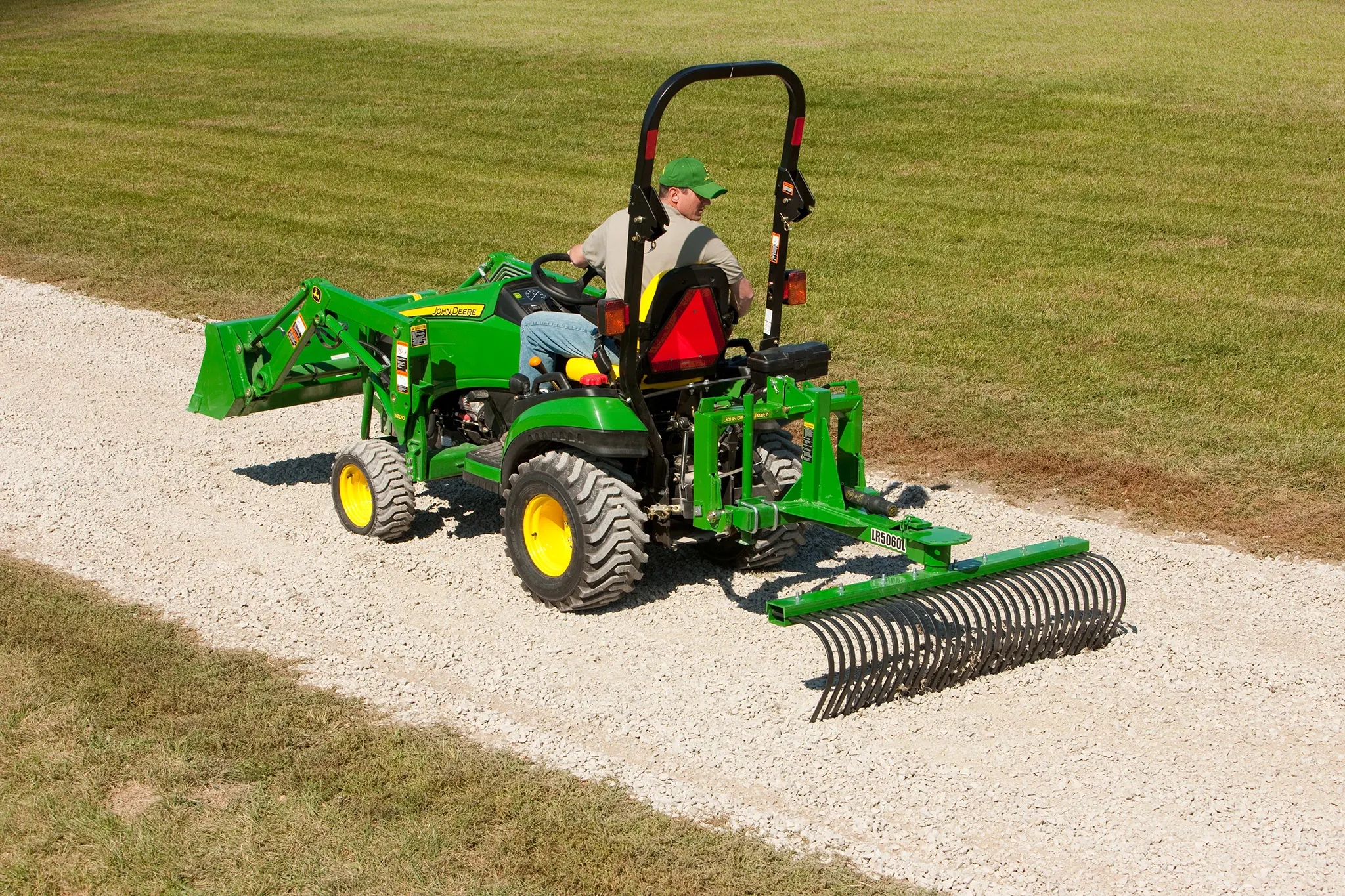 Man drives tractor pulling a landscape rake on a road