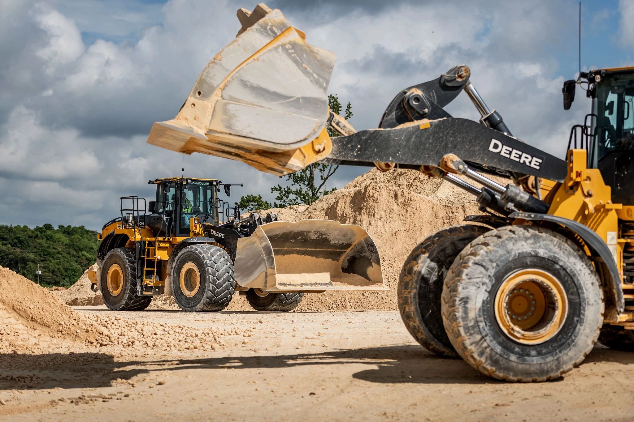 Two John Deere construction wheel loaders driving around a gravel pit