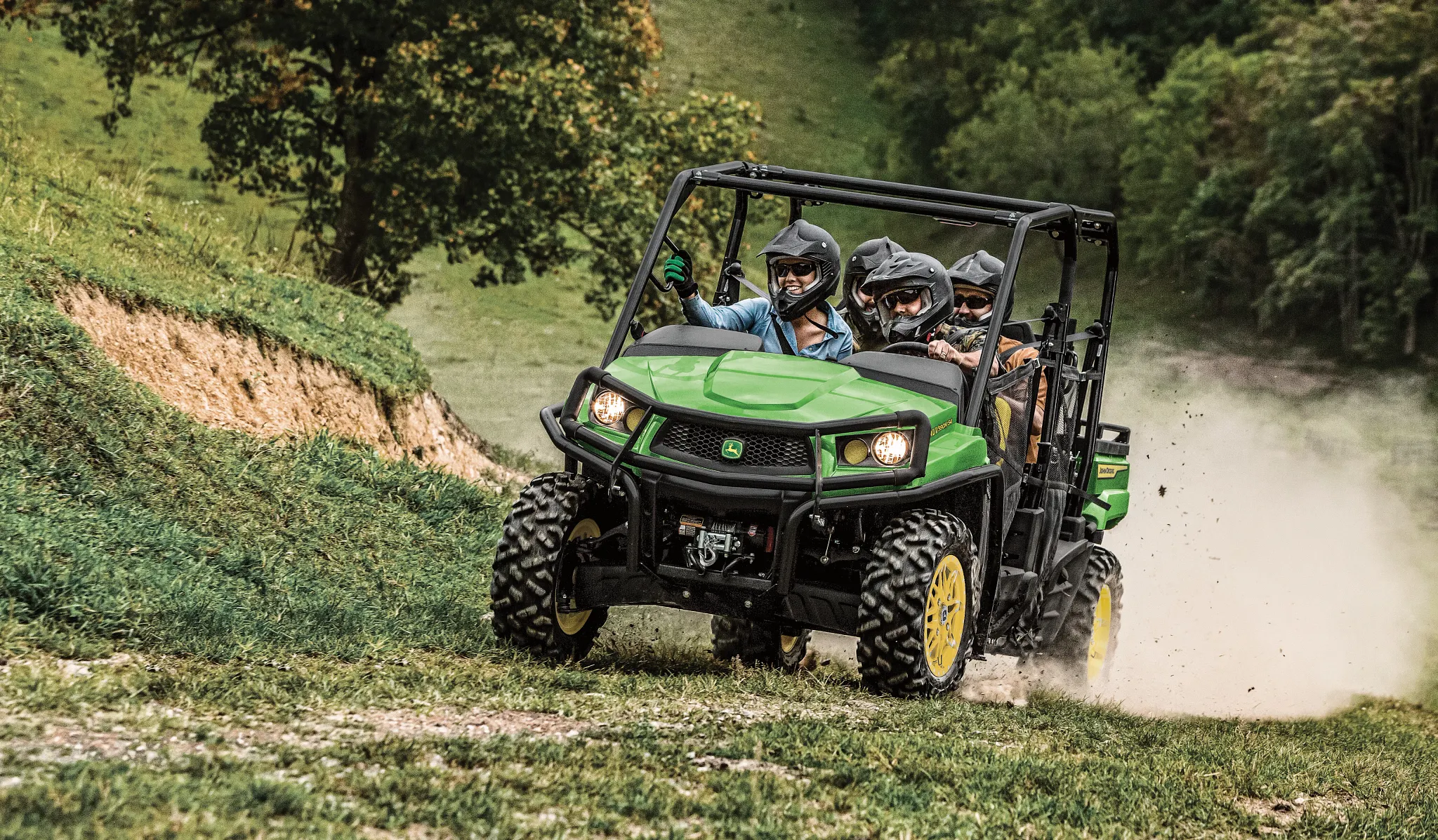 Front left view of an XUV 590M S4 Gator with four helmeted passengers tearing down a grassy path, dust flying behind it