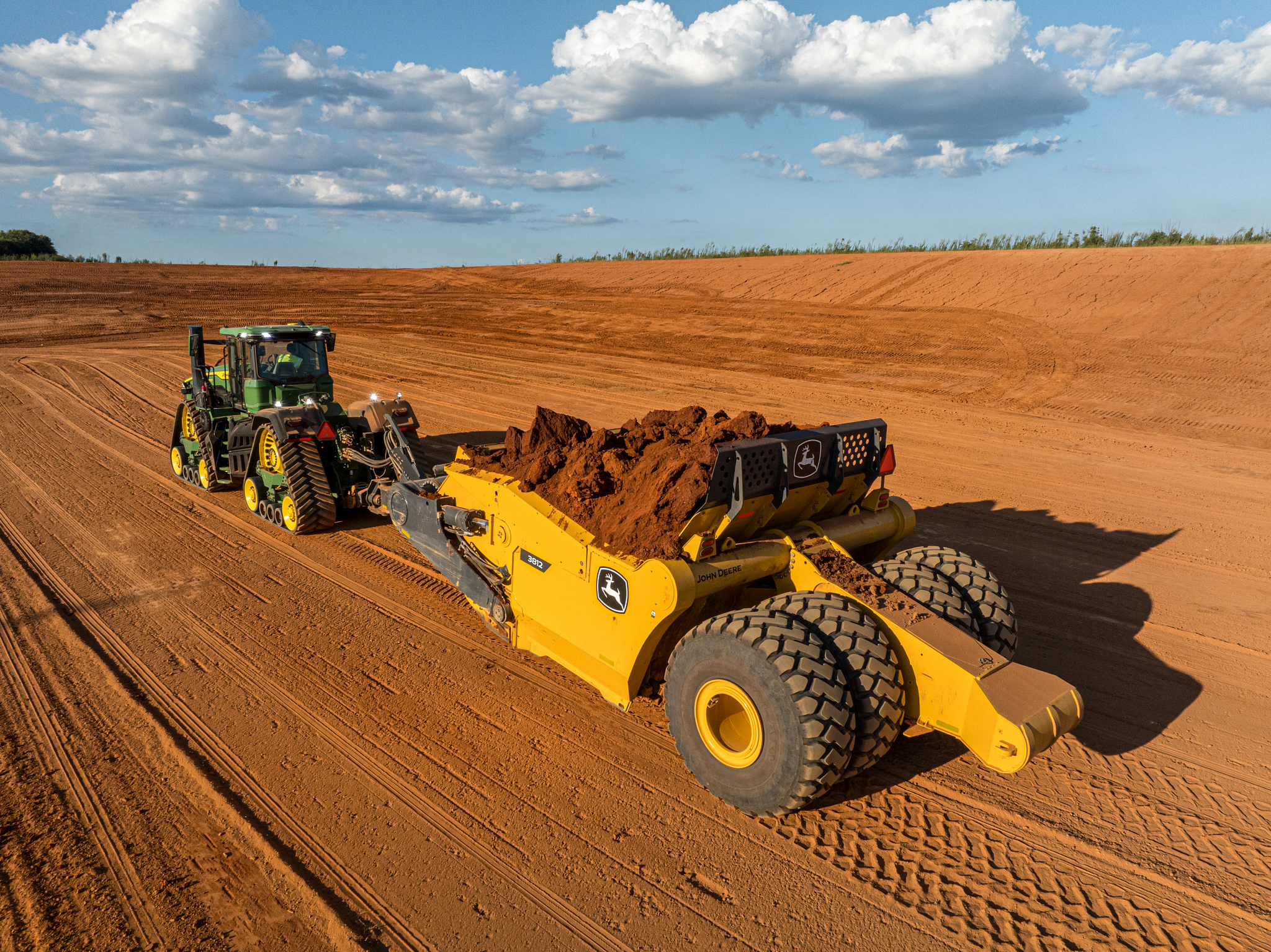 Rear left view of a 9RX 770 Scraper Special Tractor and 3812 Scraper mounded with dirt traveling across an expanse of red dirt