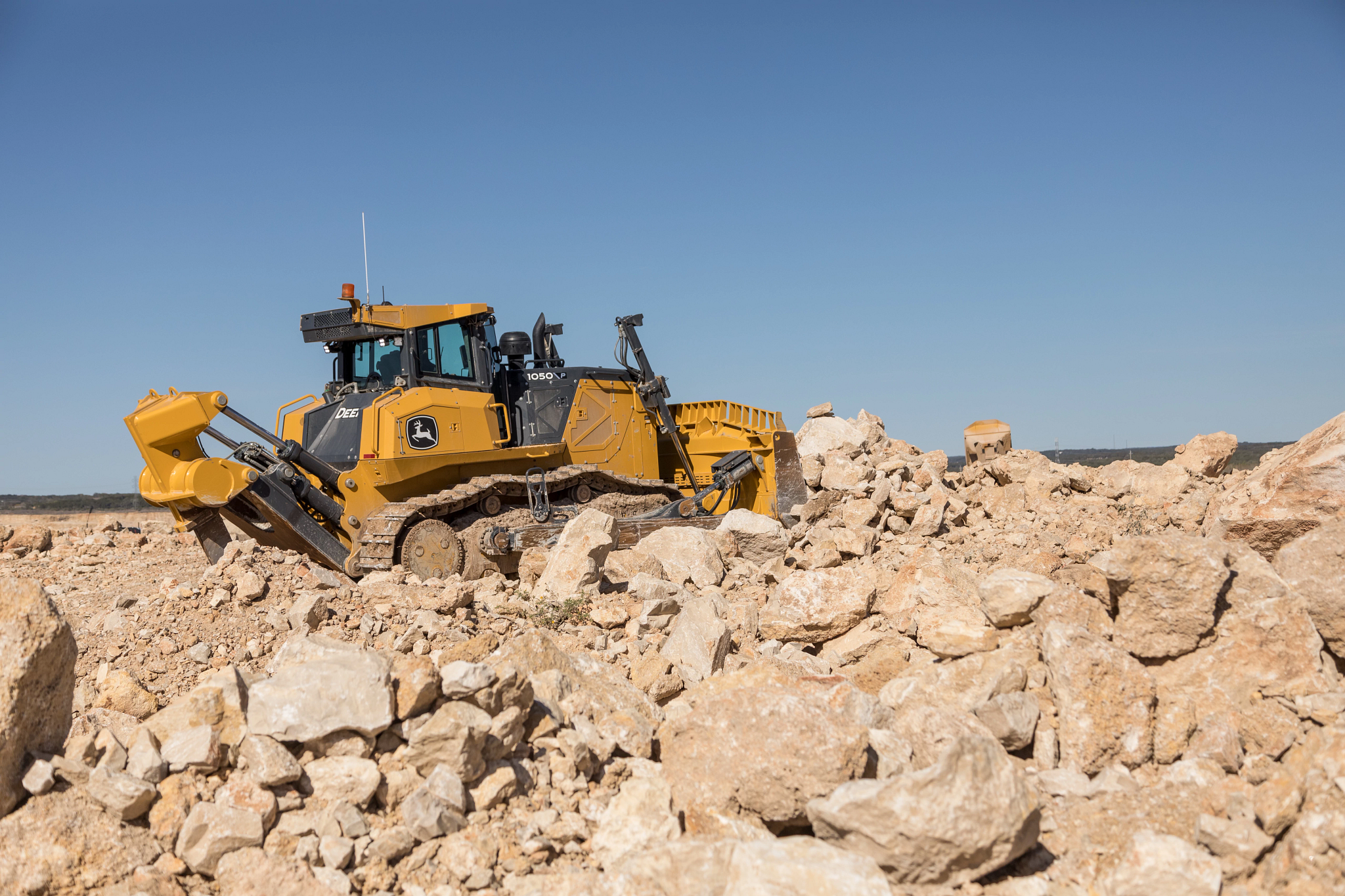 Rear right view of an orange construction 1050 P-Tier dozer pushing boulders around a rock field