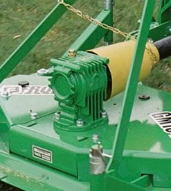 Close-up of a green gearbox with cooling fins mounted on a grooming mower, connected to a yellow PTO driveline and secured with metal supports