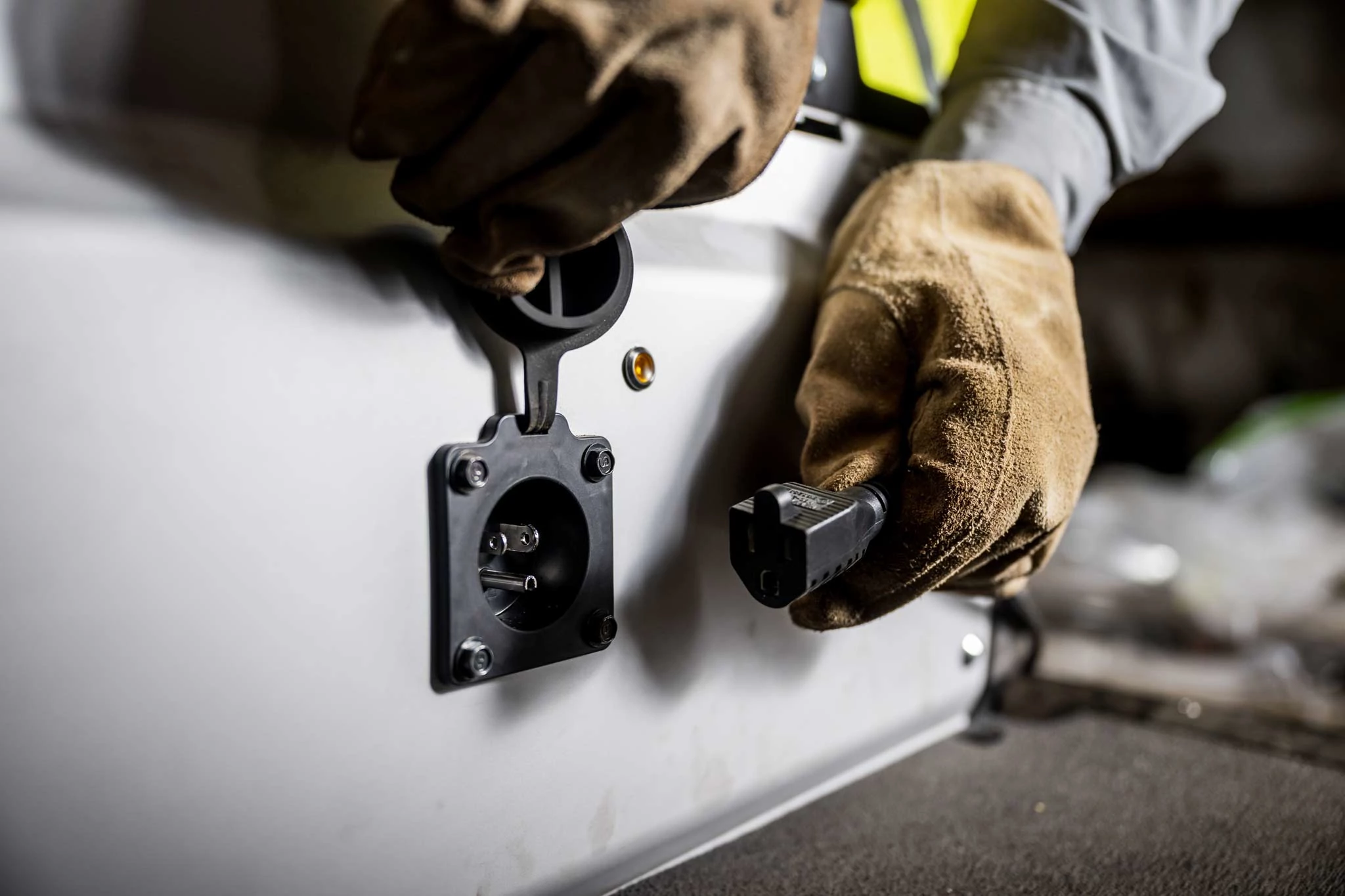 Close-up of two gloved hands opening the GX Electric charging plug, making to plug a cord into the uncovered port