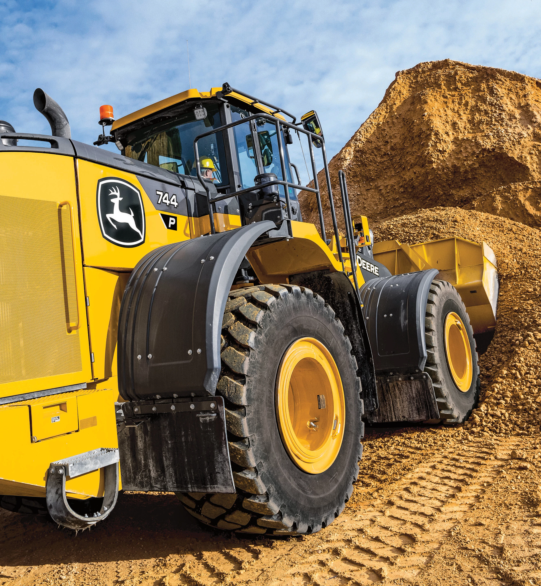 Close-up view of a large yellow front-end loader parked at a quarry, positioned beside a tall mound of gravel