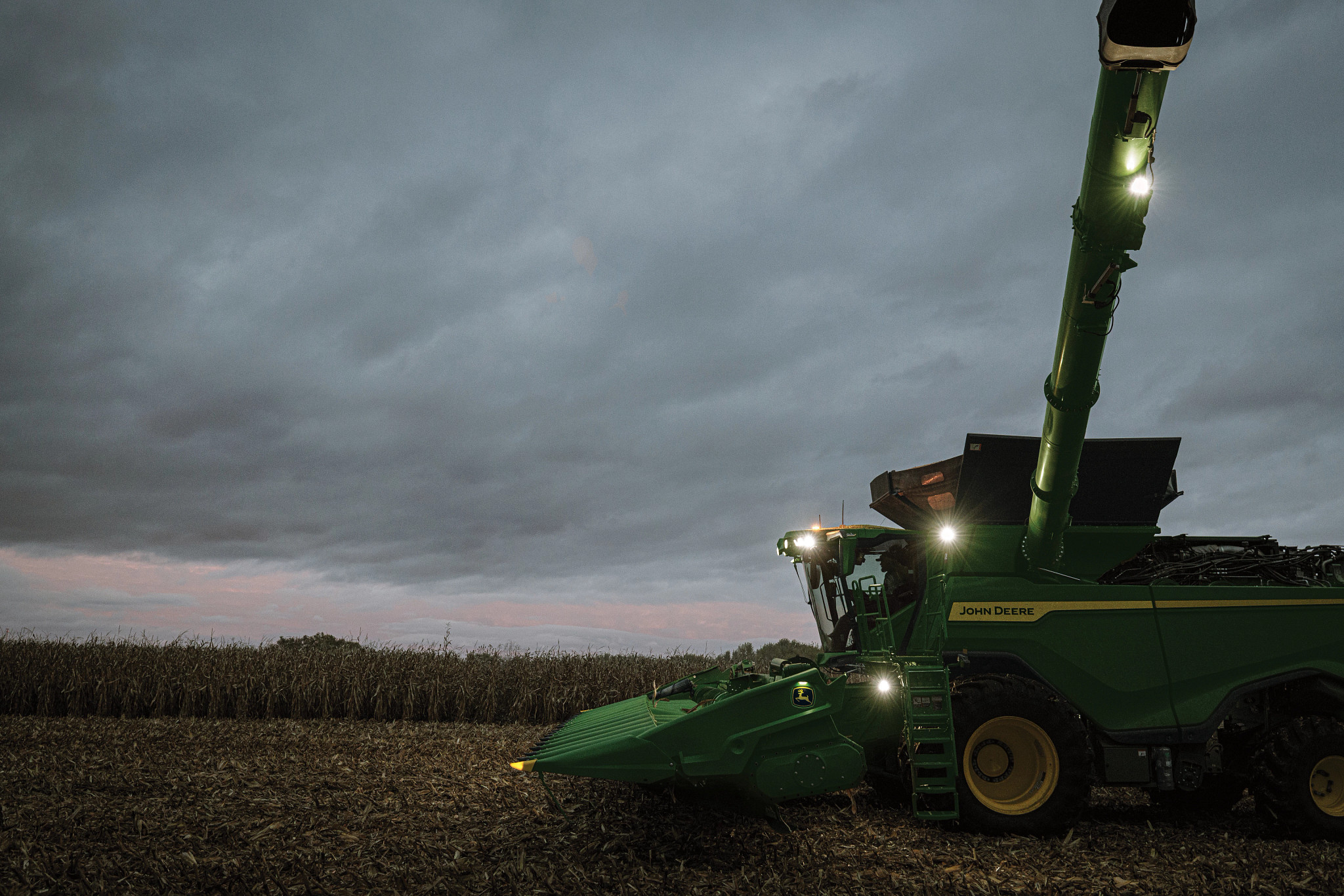 John Deere combine harvesting corn at dusk
