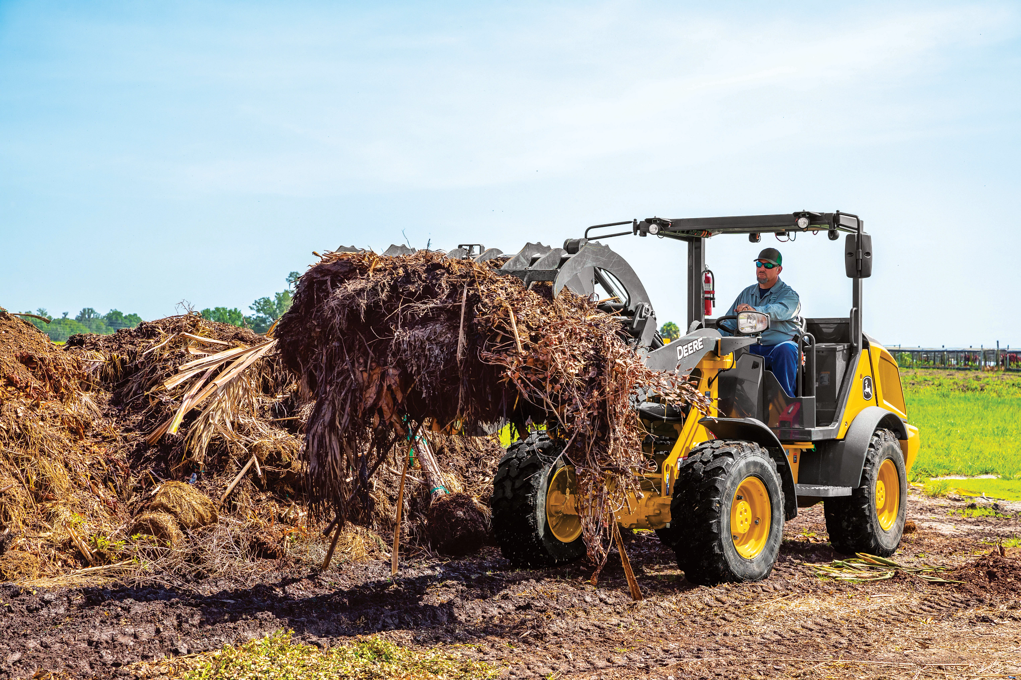 Front left view of a 184 G-Tier compact wheel loader being driven by an operator picking up brush