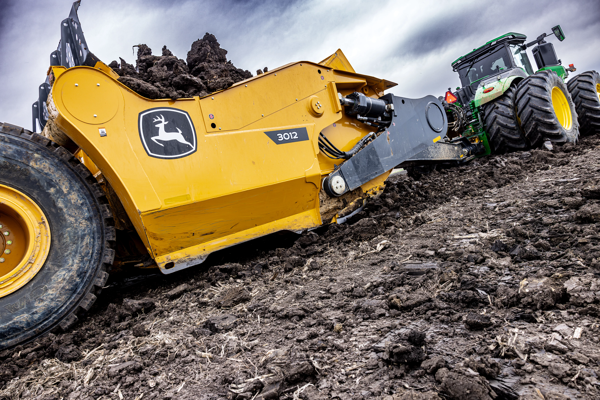 Side rear view of a 3012 large direct hitch scraper loaded with dirt being pulled by a 9R 640 scraper special tractor