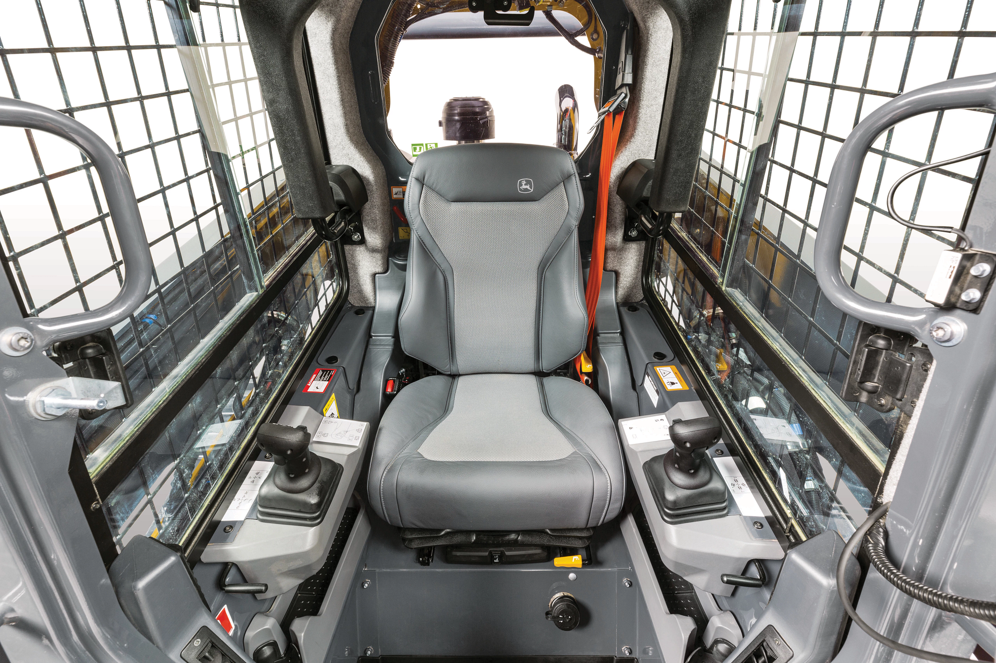 Interior cab view of a skid steer loader showing a central padded operator seat, protective side grid panels, and dual joystick controls on both armrests