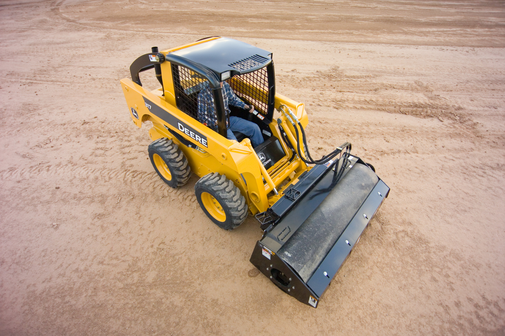Overhead front right view of smooth drum vibratory roller mounted to the front of a skid steer in a large dirt field