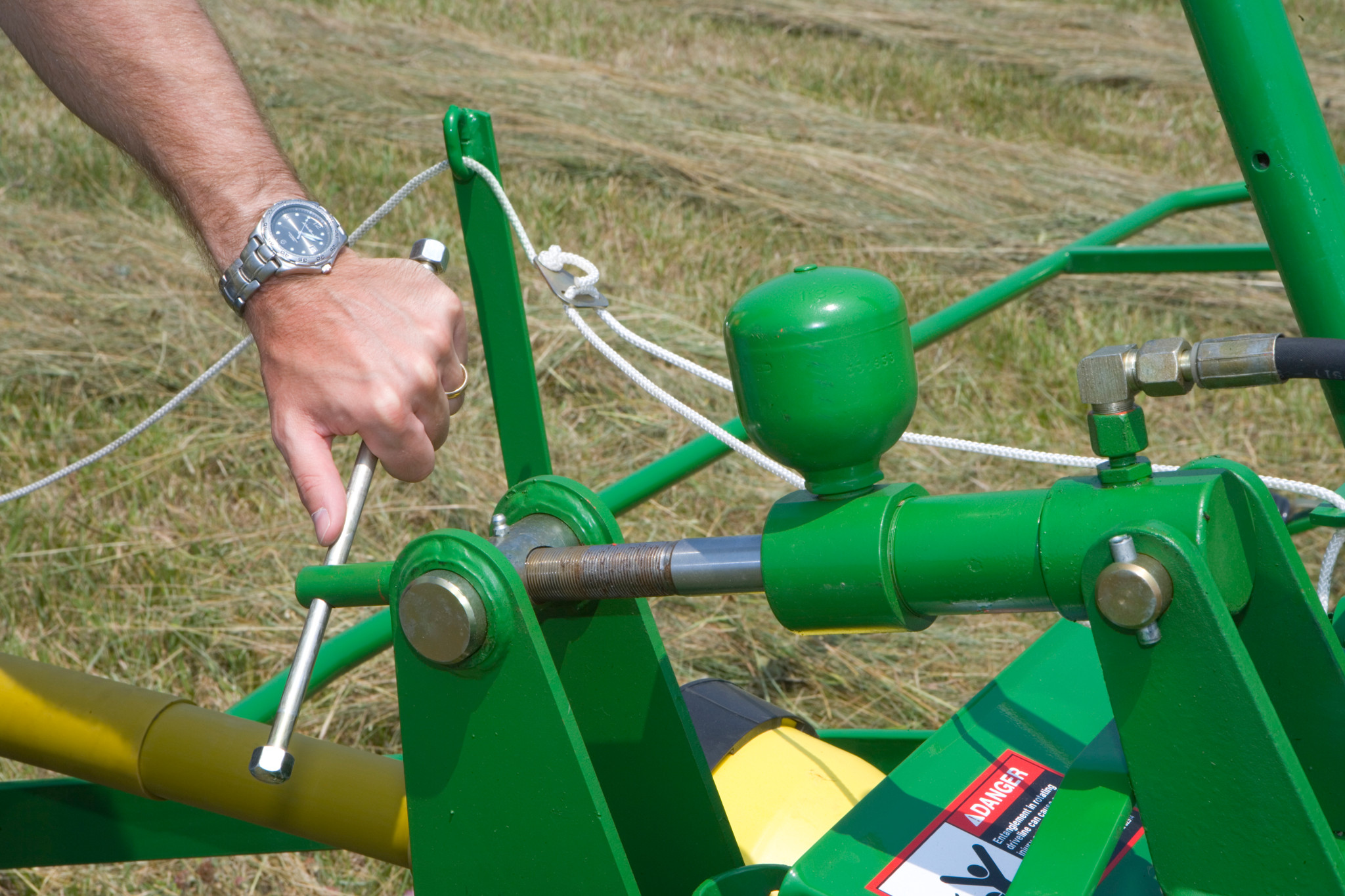 A man's hand turning a rotor adjustment handle at the front of the TD13 Hay Tedder