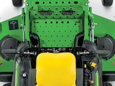 Top‑down view of zero‑turn mower showing the operator area with a yellow seat, control levers, perforated deck surface, and twin mower housings on either side.
