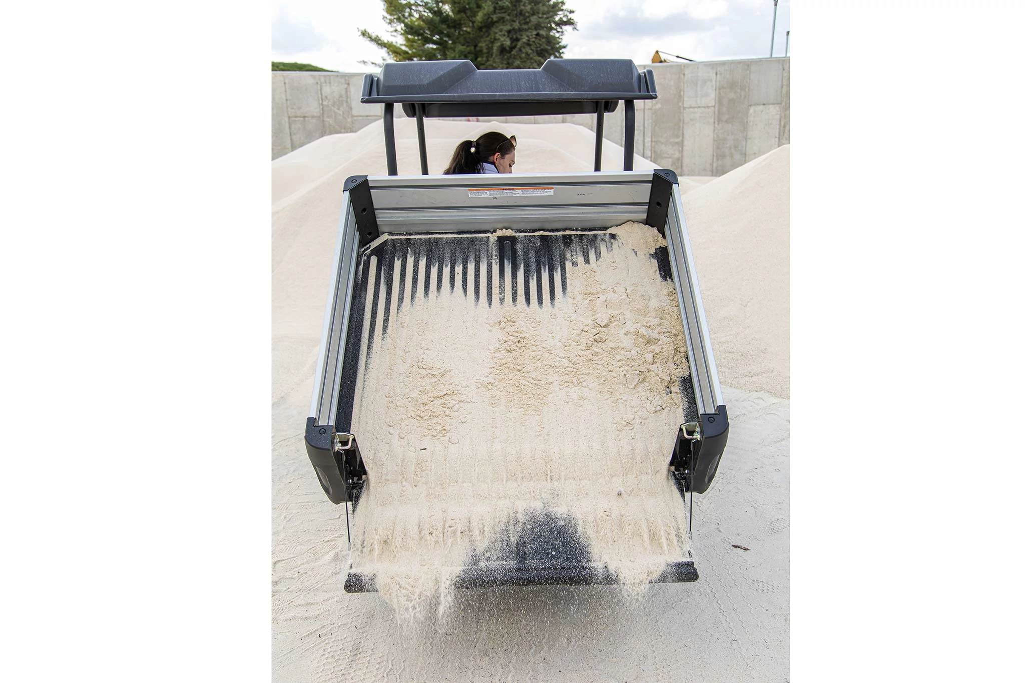 Rear view of a GS Electric Gator dumping sand from its bedliner with tailgate open.