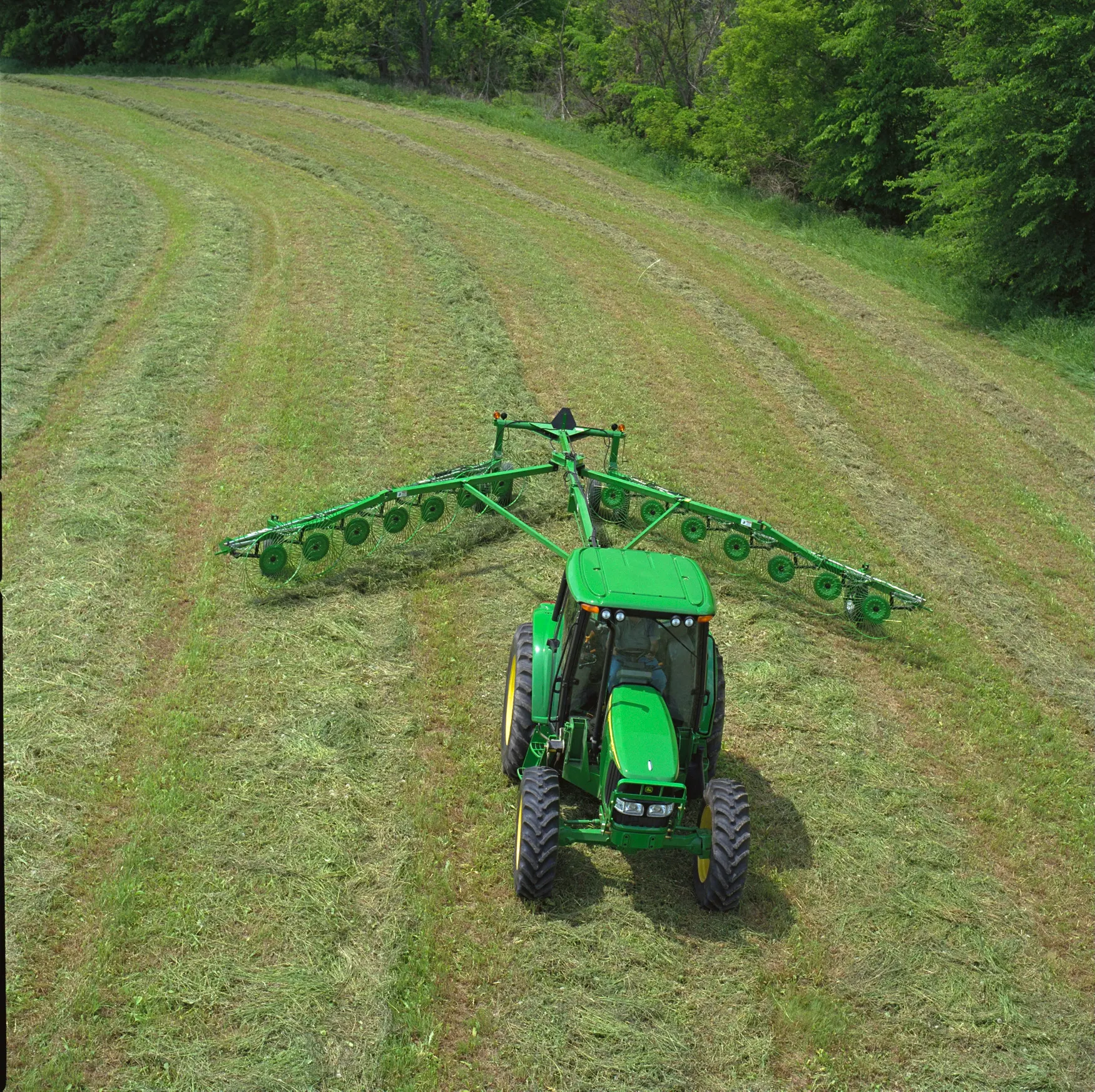 Top view of a green tractor pulling a WR1214 High-Capacity Wheel Rake across a grass field