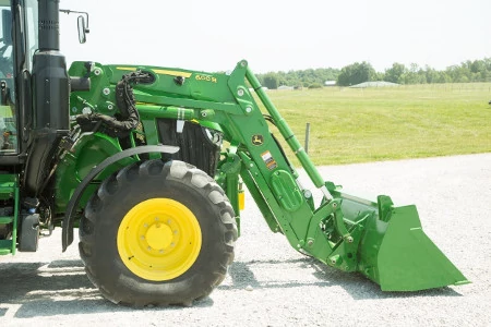 Side right view of the front half of a tractor with attached 600R loader bucket resting on gravel in front of a grassy field