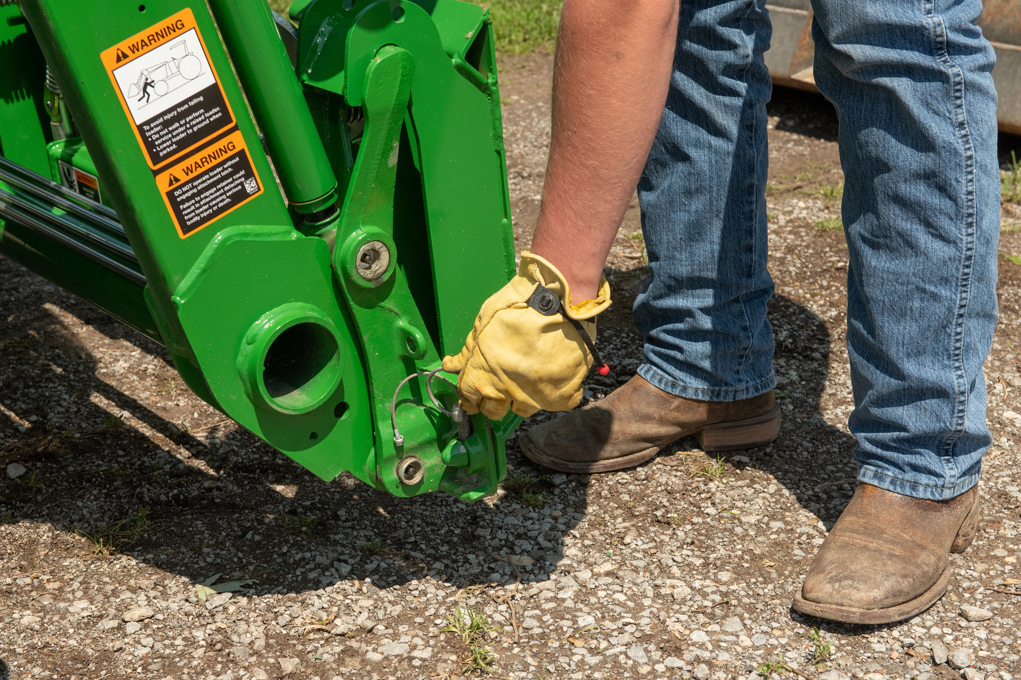 Close-up of a farmer's jeaned legs and gloved hand locking an SA20F skid steer carrier adapter into place on a 3038E compact utility tractor