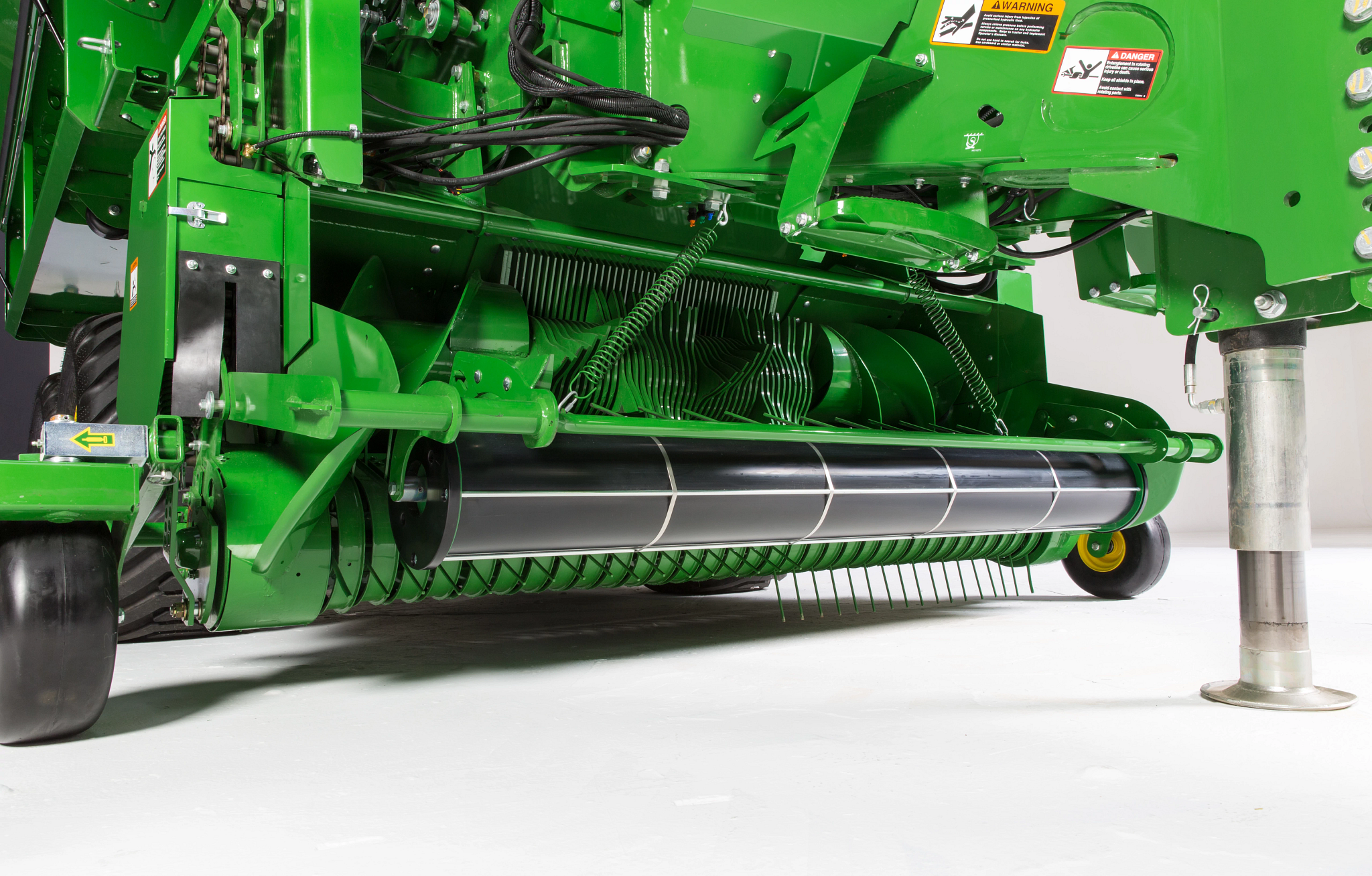 Lower front view of a green agricultural baler showing the pickup reel with tines, roller, and surrounding frame components