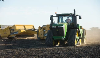Tracked tractor and scraper system making a turn on an expanse of dirt.