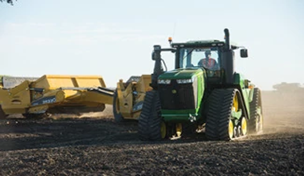 Tracked tractor and scraper system making a turn on an expanse of dirt.