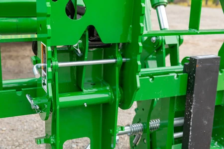 Close-up of a tractor implement hitch assembly showing steel mounting brackets, linkage arms, adjustment rods, bolts, and hydraulic components.