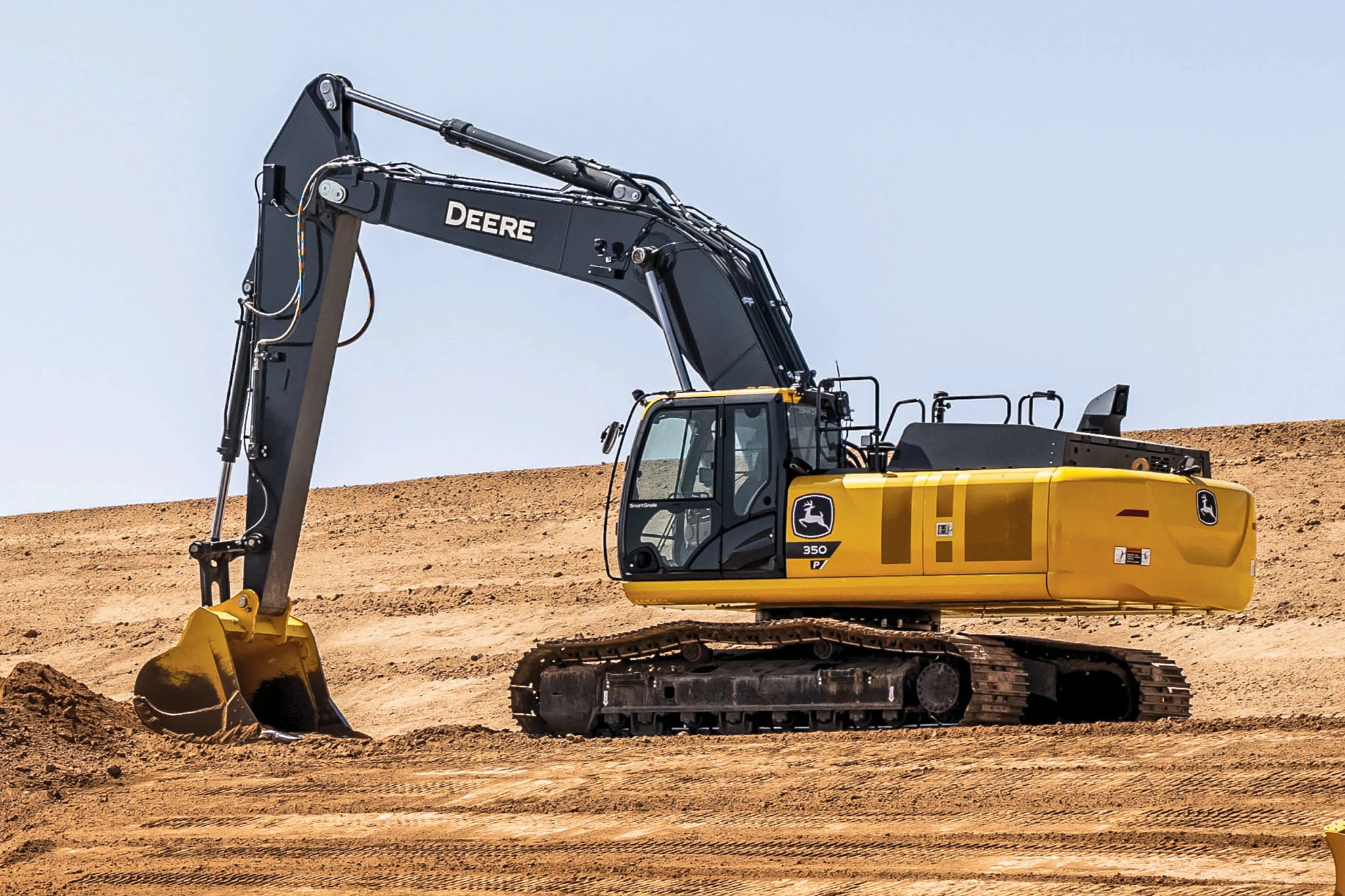 Yellow John Deere 370 excavator with a black arm and bucket positioned on flat, sandy terrain at a construction site