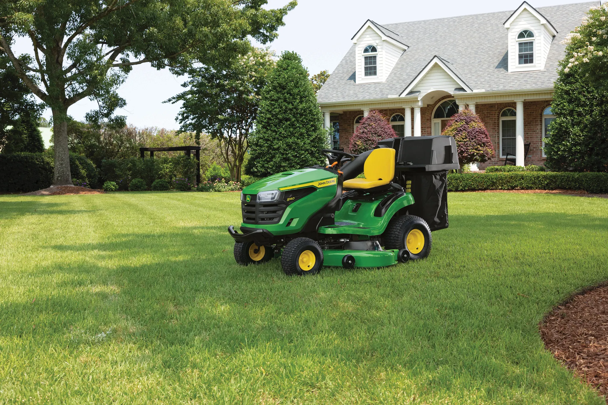 Front left view of an S140 Lawn Tractor with material collection system resting on a residential lawn