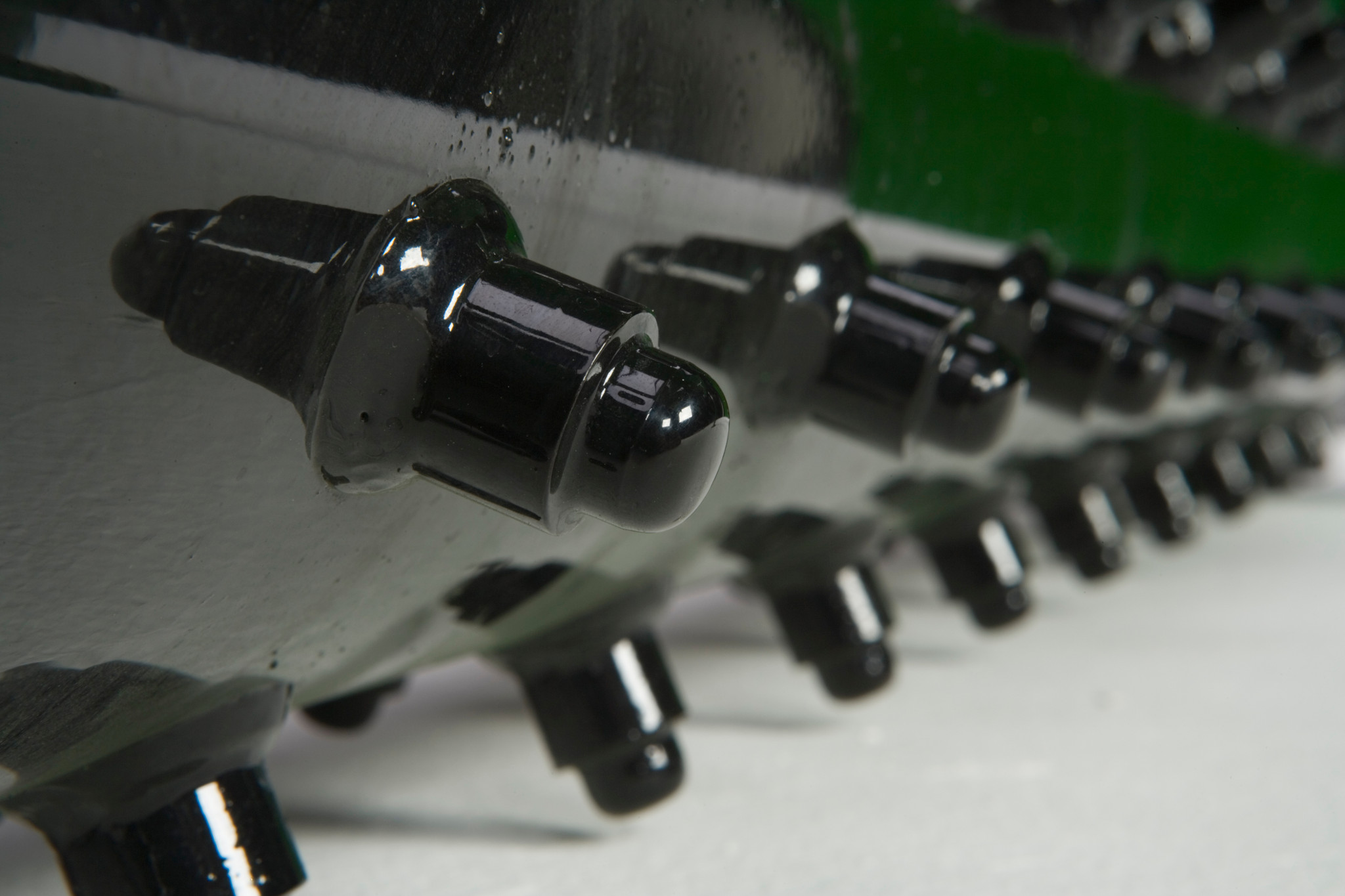Close-up of a row of black carbide cutting teeth mounted along the edge of a rotating drum