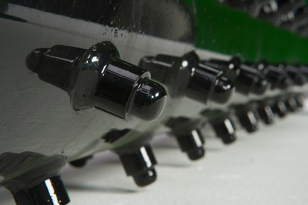Close-up of a row of black carbide cutting teeth mounted along the edge of a rotating drum