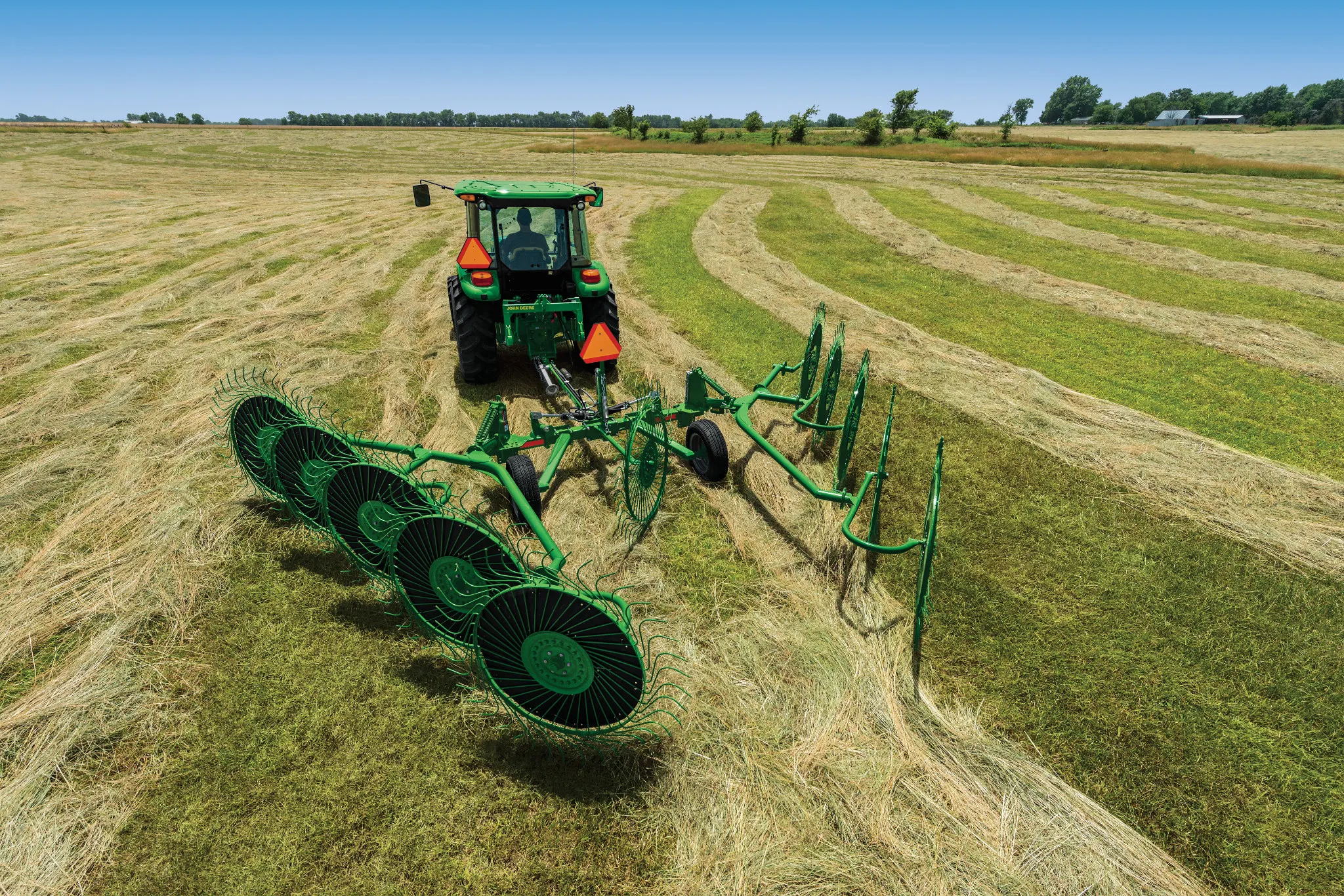 Rear view of a 5M tractor with attached WR0010 Wheel Rake working in a green and tan field