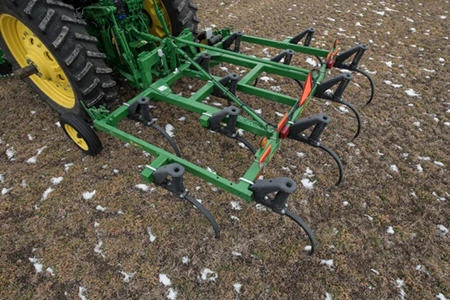 Close-up top view of a 610 chisel plow and rear tractor wheels as it travels across a brown, snow-flecked dirt field