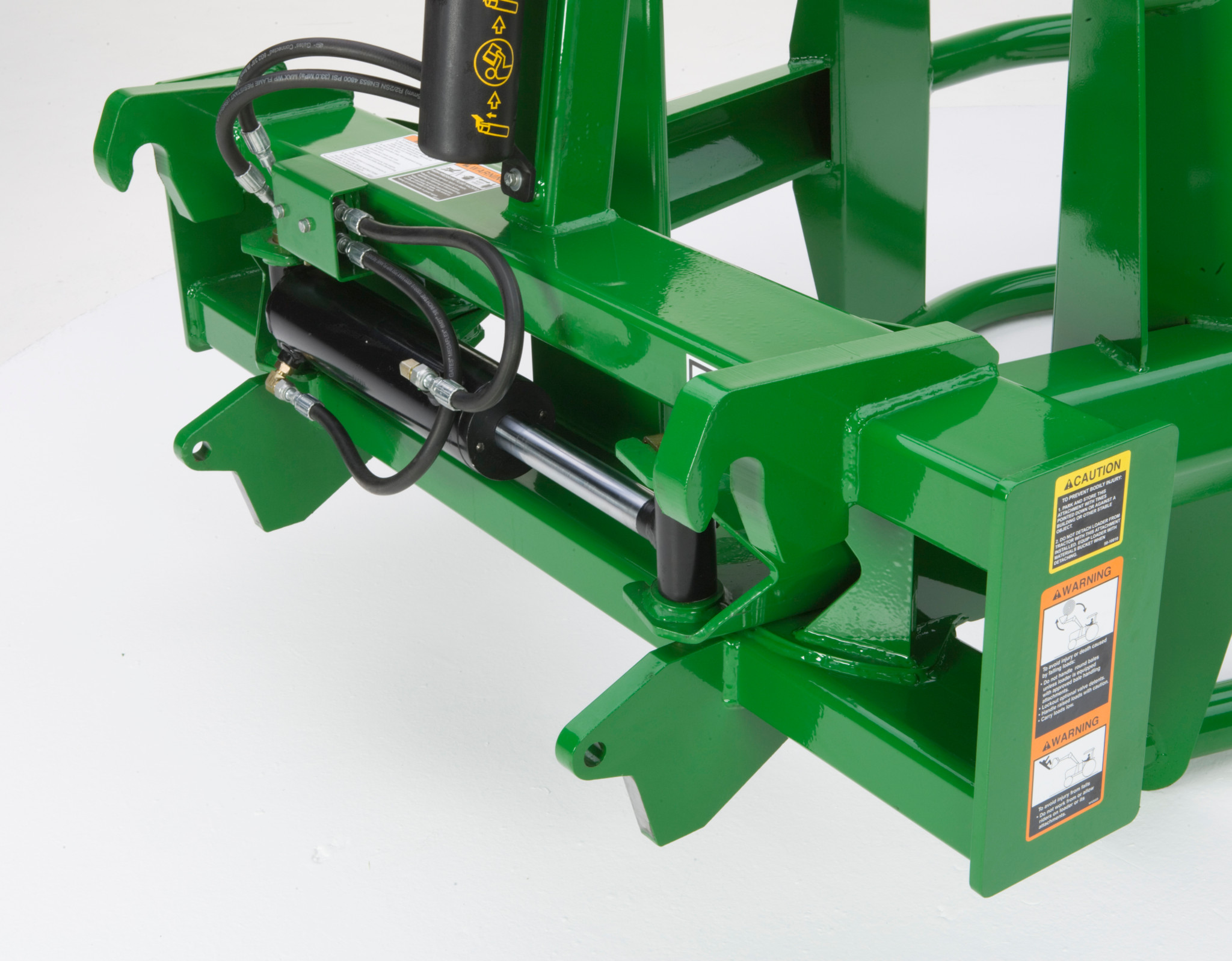 Close-up of round bale hugger showing hydraulic cylinders, hoses, and mounting brackets on the front frame