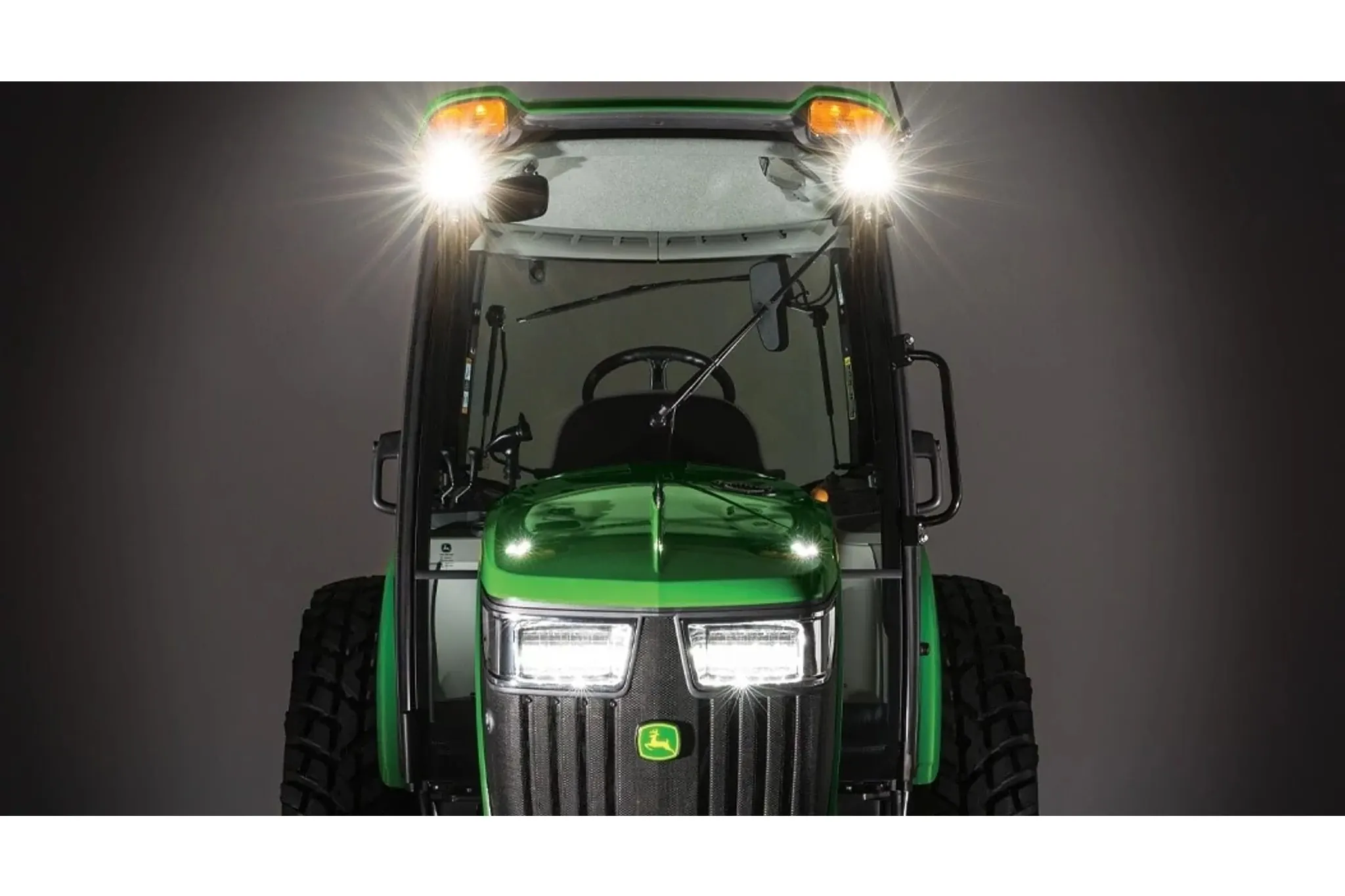 Front view of tractor in dark studio, highlighting the bright LED lights on top of cab and front of engine.