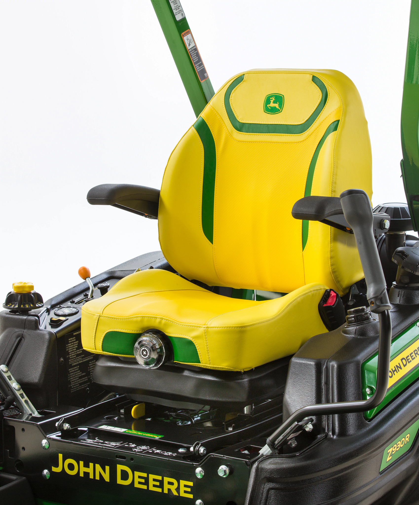 Close-up of mower seat with green accent panels and armrests, mounted on a black equipment frame with visible seat adjustment knob, control levers, and roll bar behind.