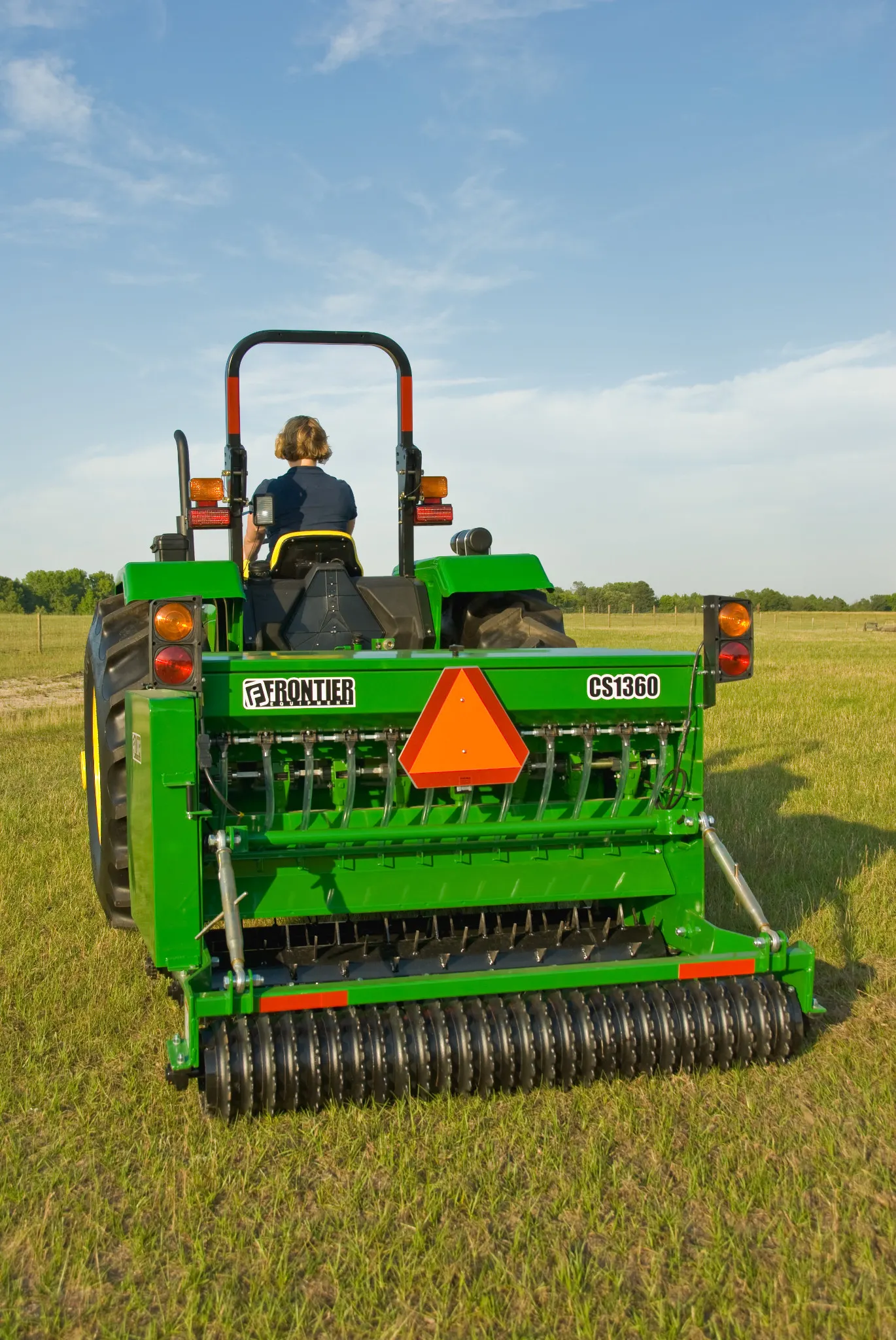 Woman pulling CS1360 Conservation Seeder with a tractor through a field