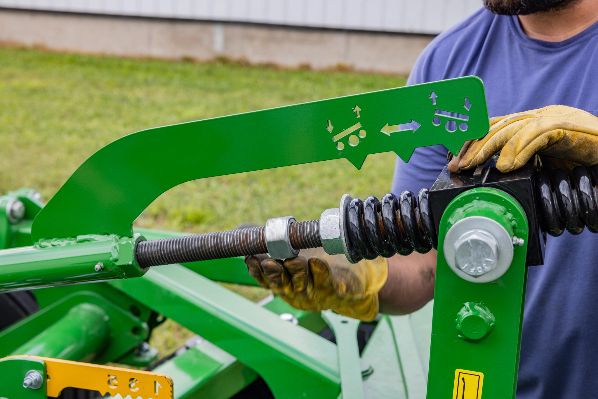 Close‑up of a green farm implement showing a threaded adjustment rod with spring as the tension mechanism is adjusted.