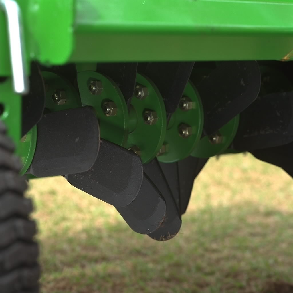 Close-up of angled paddles mounted on a rotating drum beneath a green overseeder implement