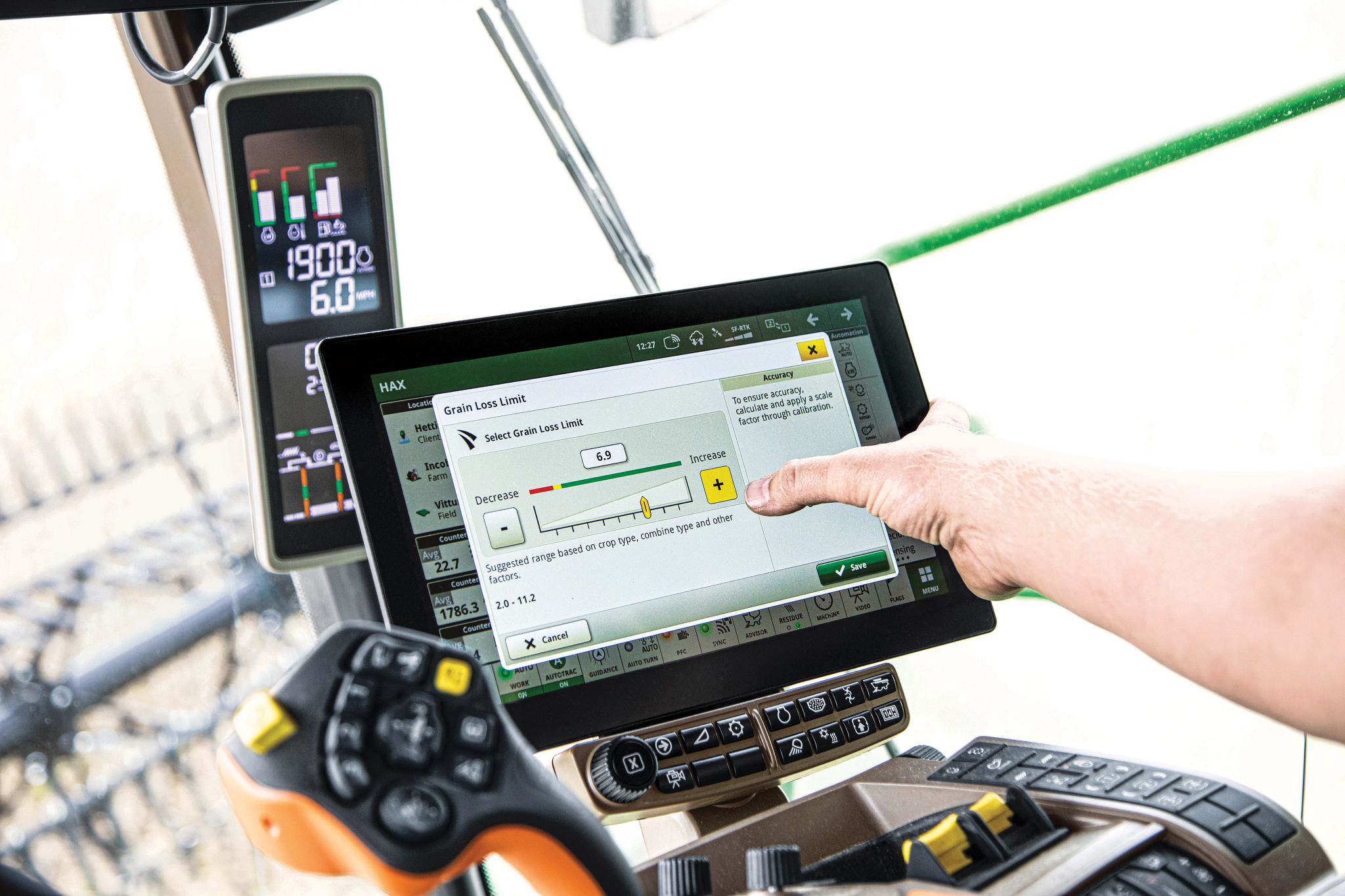 A hand and arm reaches from the right side of the shot to touch a display in an X9 1100 combine's operator station