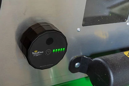 Close-up of a fill sensor mounted on a material collection system, showing green LED status lights indicating system operation