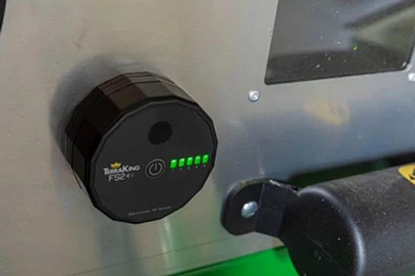 Close-up of a fill sensor mounted on a material collection system, showing green LED status lights indicating system operation