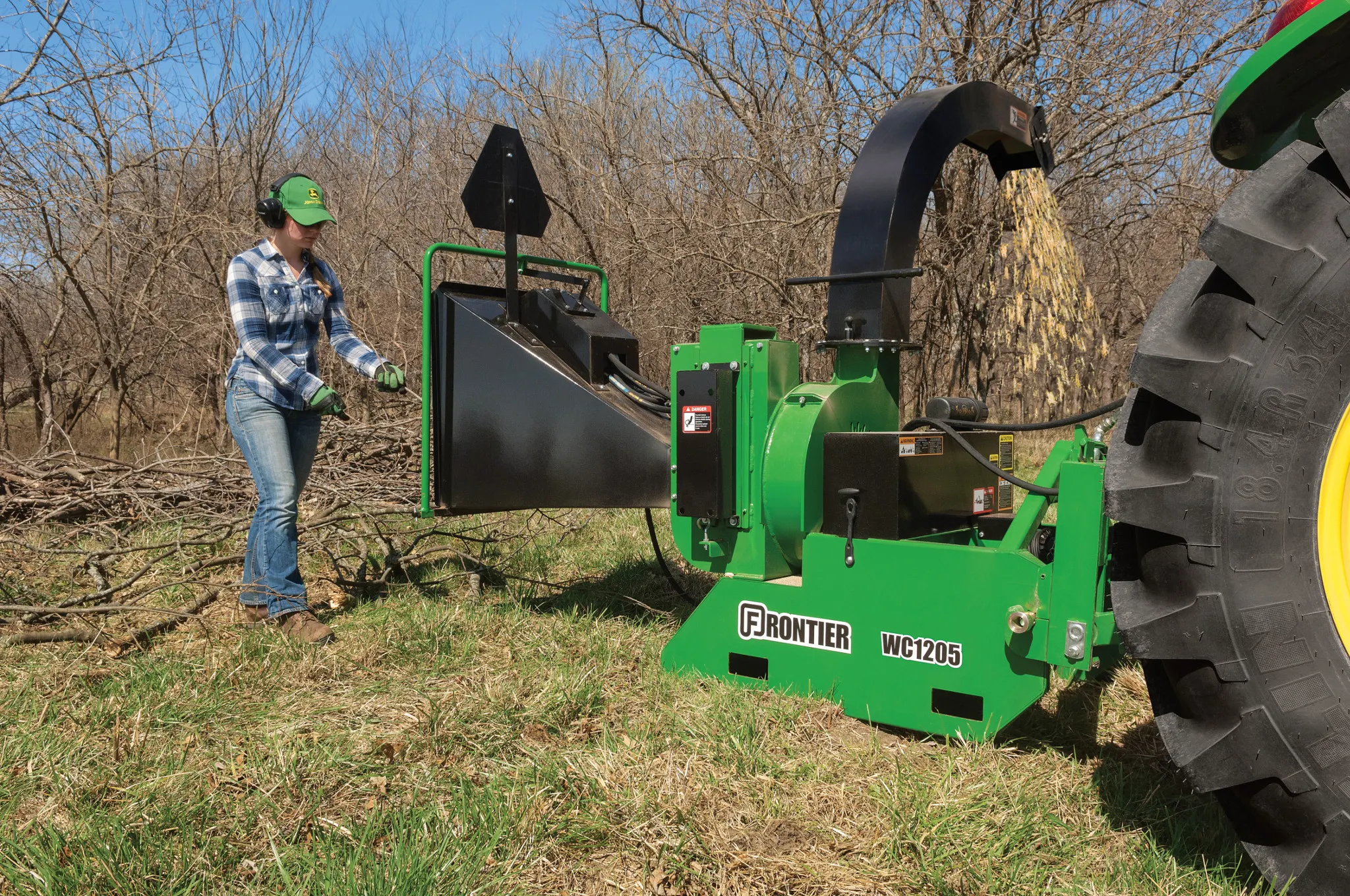 Woman loading branches into a WC1205 Wood Chipper along a tree line